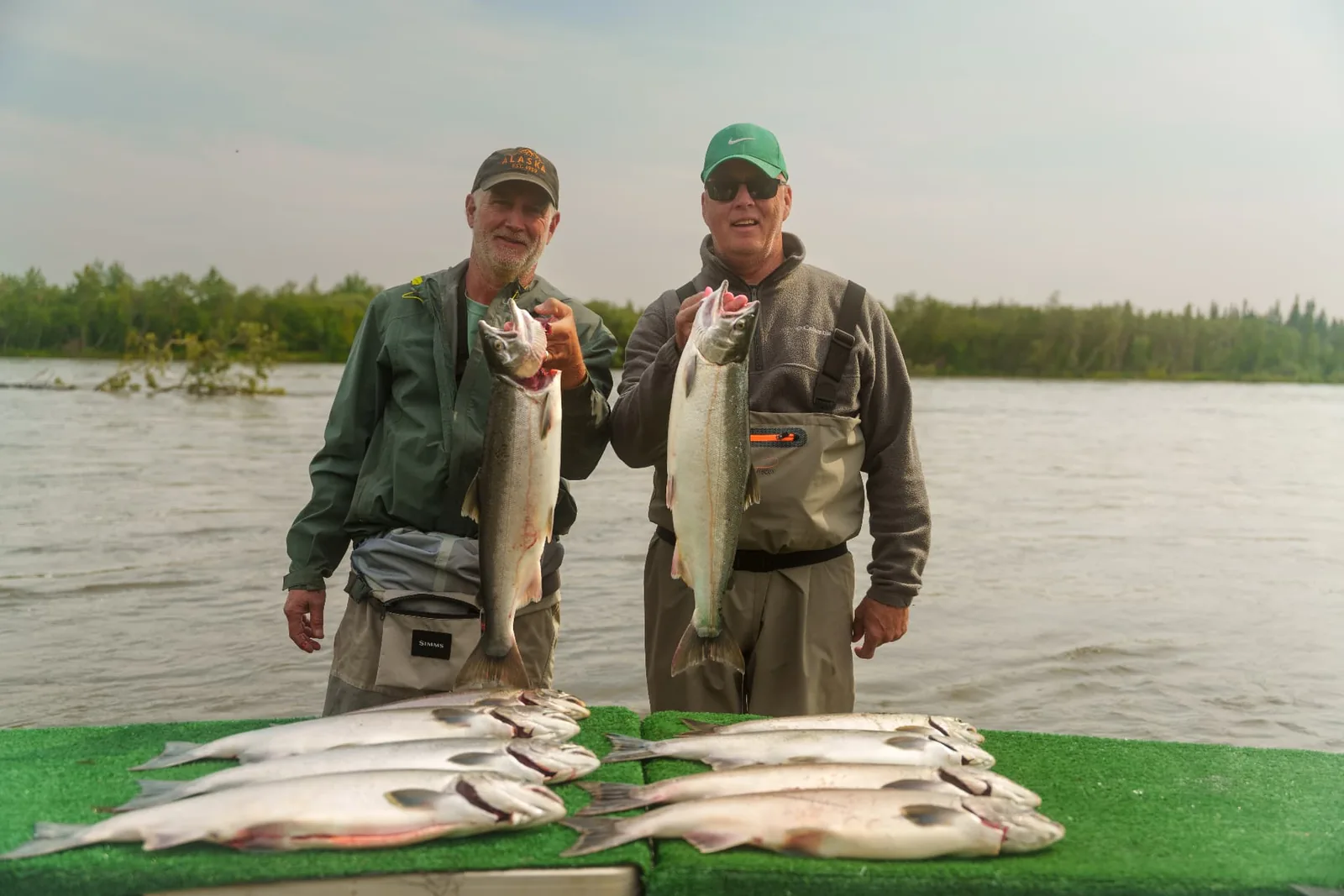 Two anglers holding salmon beside their catch on the Mulchatna River