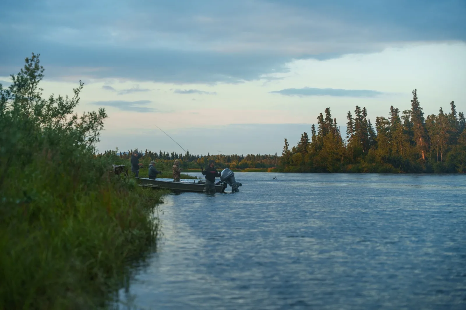 Anglers fishing from a boat at the river's edge at dusk on the Mulchatna River