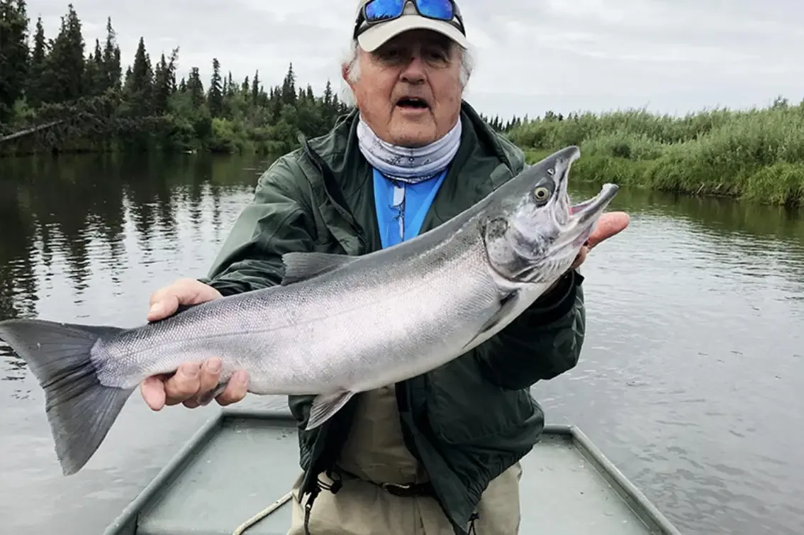Angler on a boat holding a silver salmon beside the river