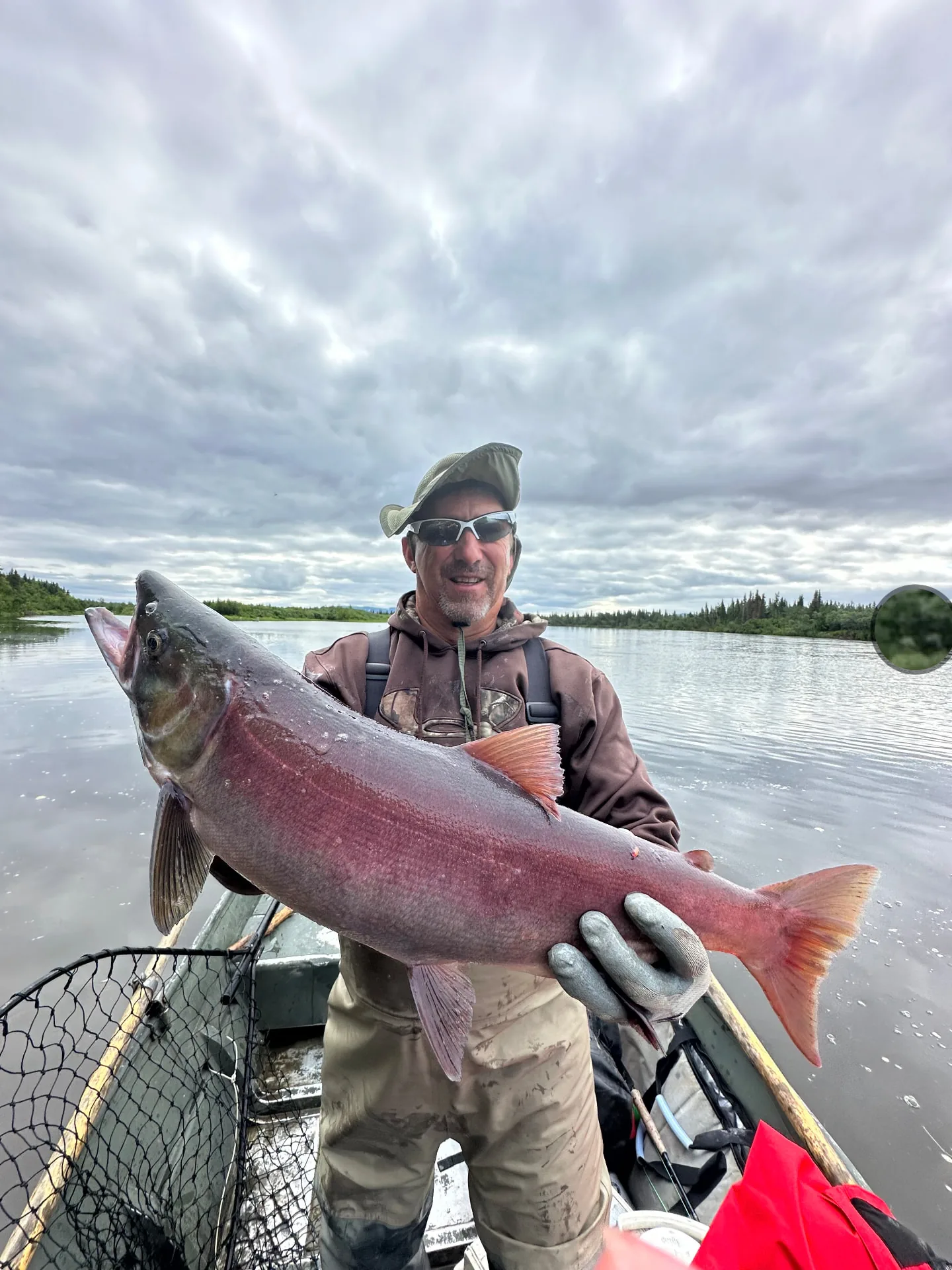 Angler in a camo hoodie holding a large sockeye salmon aboard the boat